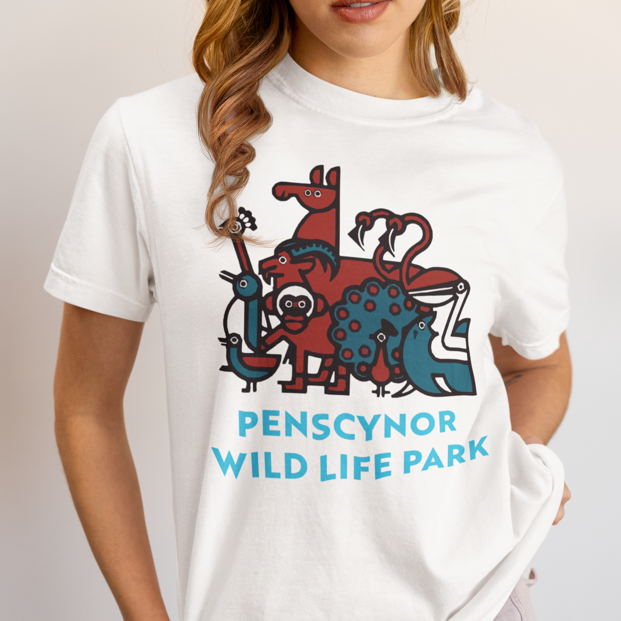 A person wearing a white crew neck t-shirt with a colorful front print that includes animals and the text 'PENSCYNOR WILD LIFE PARK'.