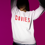 Person wearing a white sweatshirt with 'DAVIES' printed on it against a pink background