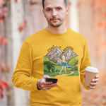 Man wearing a yellow sweatshirt with a nature graphic, holding a coffee cup and phone, standing in front of autumn foliage.