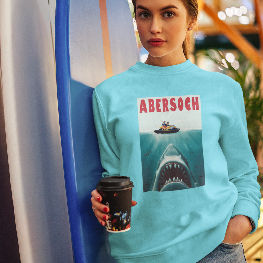 Person wearing a blue sweatshirt with a shark graphic and 'Abersoch' text, holding a coffee cup.