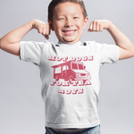 A young boy smiling and flexing his biceps, wearing a light gray graphic t-shirt with a red truck design and the text 'HOT DOGS FOR TEA BOYS', blue jeans, and blue sneakers, against a light gray studio background.