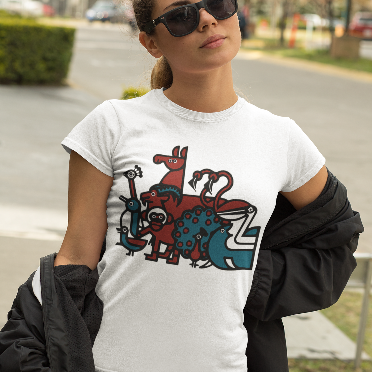 A woman wearing a white graphic t-shirt with a colorful illustration of the Penscynor logo, styled with a black jacket draped off her shoulders and sunglasses, set against an outdoor street background.