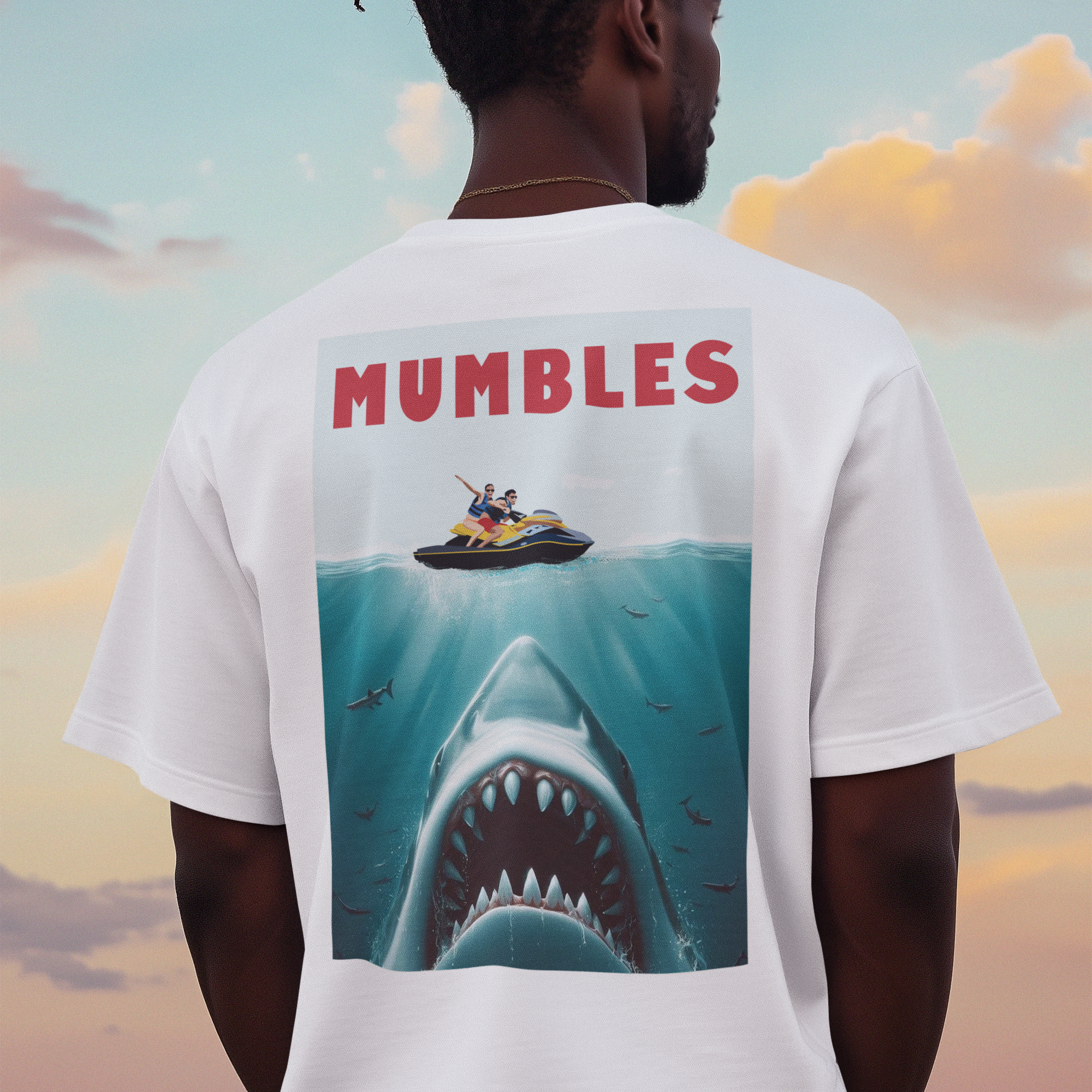 Person wearing a white t-shirt with a shark graphic and 'Mumbles' text, standing against a colorful sky.