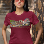 A woman wearing a maroon short-sleeve graphic t-shirt and beige pants, standing outdoors against a stone wall.