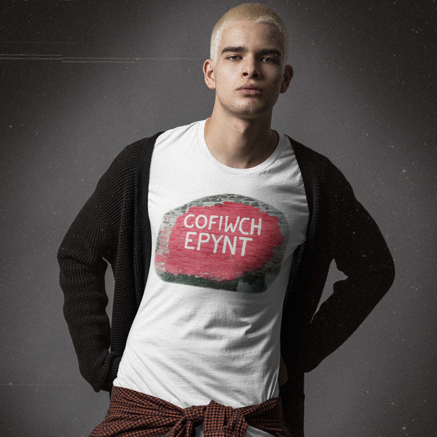 Person wearing a white t-shirt with a Cofiwch Epynt design and a dark cardigan over shoulders on a gray background