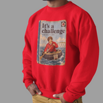 A man wearing a bright red crewneck sweatshirt with a vintage-style graphic print on the front. The print shows a book cover titled 'It's a challenge' with an illustration of a man in a lifeboat.