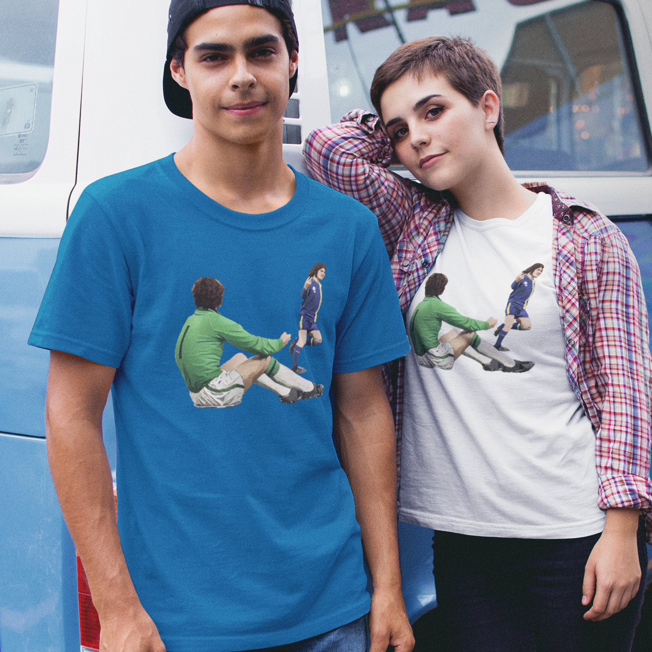 Two people wearing t-shirts with graphic designs of Robin Friday flicking the V's after scoring a goal, standing in front of a blue van.