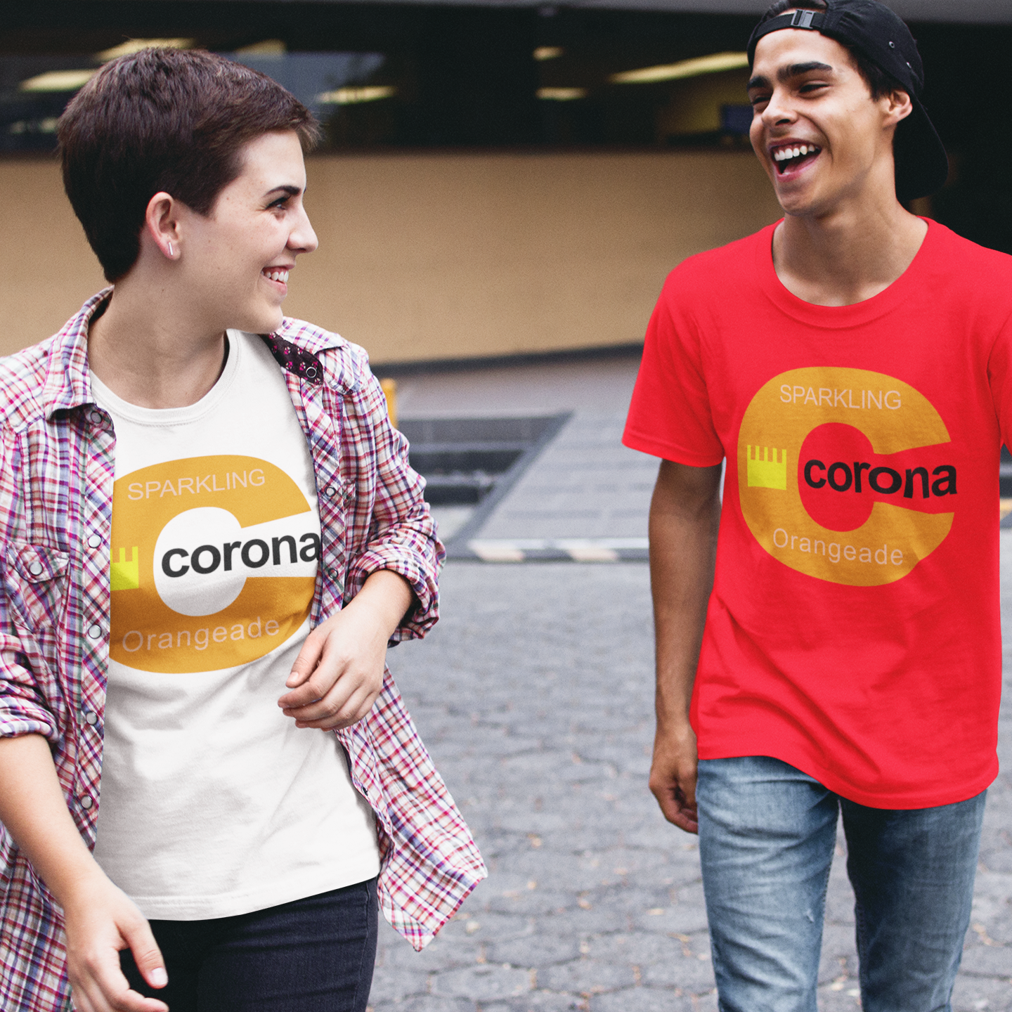 Two young men walking outdoors in a parking lot, both wearing matching red and white t-shirts with a yellow and orange circular 'corona Sparkling Orangeade' logo. The man on the left wears a red and white plaid shirt over a white t-shirt, while the man on the right wears a red t-shirt with a black baseball cap backwards.