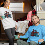 A man and a woman pose in front of a vintage beige camper van, each wearing a matching crewneck sweatshirt with a colorful Penscynor graphic. The woman wears a white sweatshirt and dark leggings, while the man wears a bright blue sweatshirt and olive green pants.