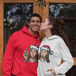 Two people standing in front of a wooden door, each wearing a hoodie with a cartoon face graphic wearing a Santa hat. The person on the left wears a bright red hoodie, and the person on the right wears a light gray hoodie.