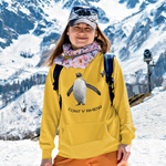 A woman posing in a snowy mountain setting, wearing a bright yellow hoodie with a penguin graphic and the text 'CONT Y RHEW', paired with orange pants and a patterned neck gaiter.