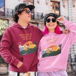 Two models posing in front of a historic building, wearing matching graphic hoodies. The model on the left wears a maroon hoodie, and the model on the right wears a light pink hoodie.