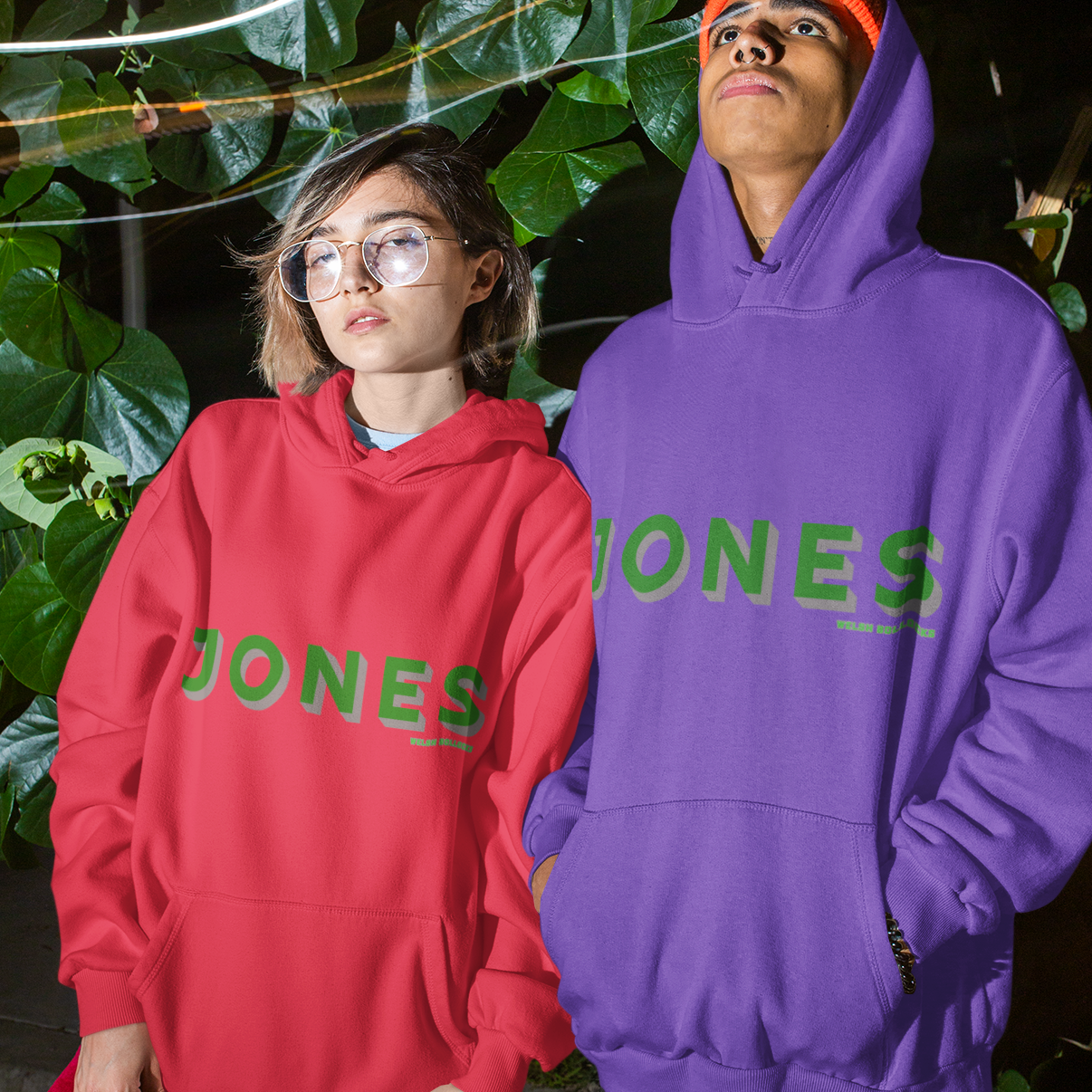 Two people wearing red and purple 'JONES' hoodies standing outdoors at night.
