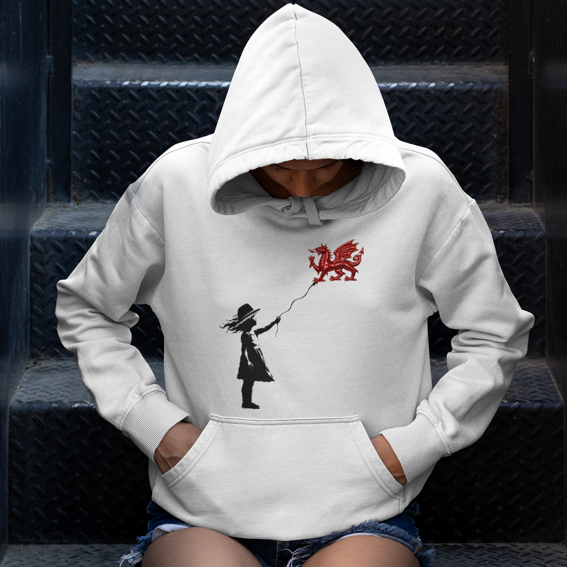 A person sitting on black diamond-plate stairs wearing a white pullover hoodie with a black graphic of a girl holding a red balloon.