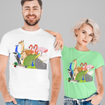 A man and a woman modeling matching graphic t-shirts against a solid gray background. The man wears a white t-shirt and the woman wears a mint green t-shirt, both featuring a colorful cartoon graphic of a giraffe, flamingos, and a green dinosaur.
