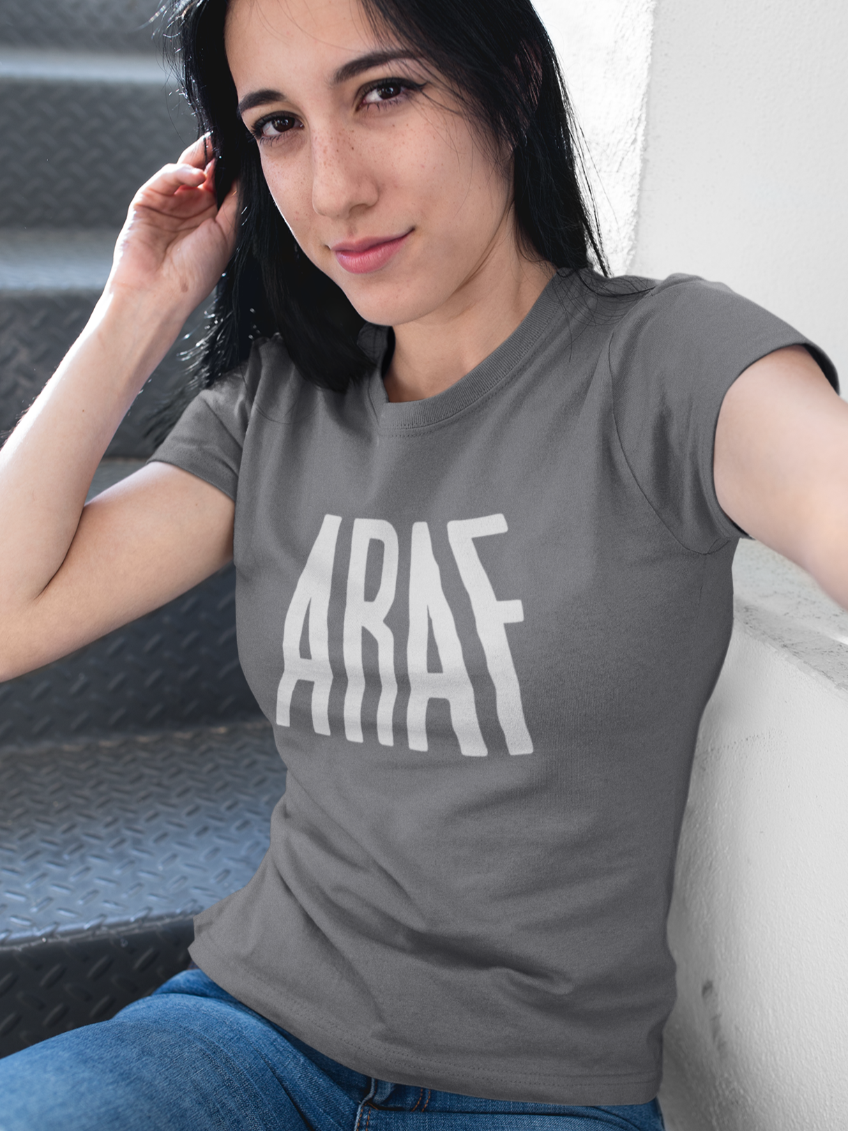Woman wearing a gray t-shirt with 'ARAF' printed on it, sitting on a couch.