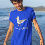 A man wearing a bright blue graphic t-shirt with a seagull illustration and the text 'Cont y sglods' standing in shallow ocean water with a beach background.