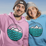 Two people wearing hoodies with a mountain and wave design outdoors.