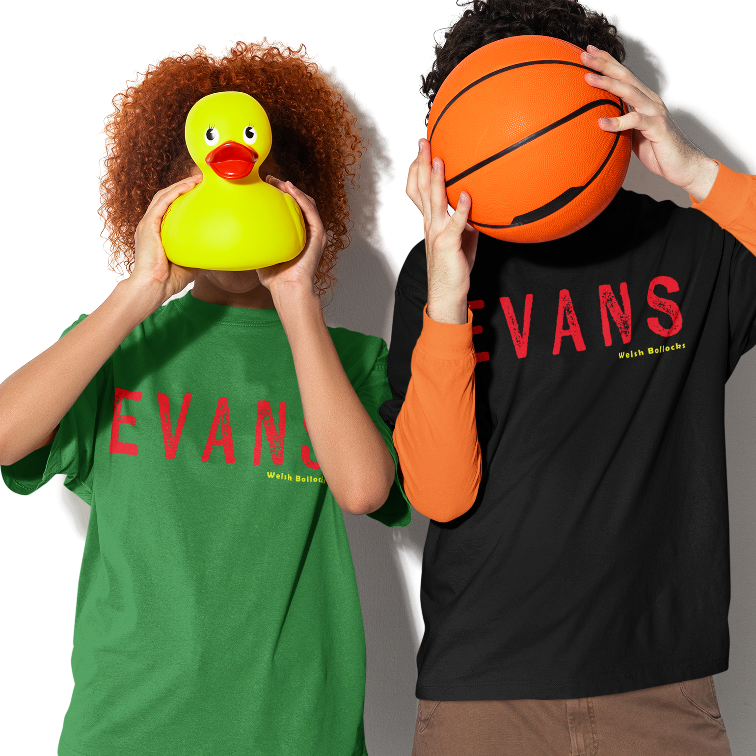 Two people wearing 'EVANS' branded shirts, one with a green shirt and blue jeans, the other with a black shirt and brown shorts, holding a yellow rubber duck and an orange basketball respectively.