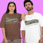 A man and a woman modeling graphic t-shirts against a solid purple background. The woman wears a brown t-shirt with a green and gray landscape graphic and the text 'PENYRONT AR OGWR'.