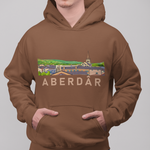 A man wearing a brown pullover hoodie with a colorful graphic of a town and the text 'ABERDÁR' across the chest, paired with blue jeans, against a solid gray background.
