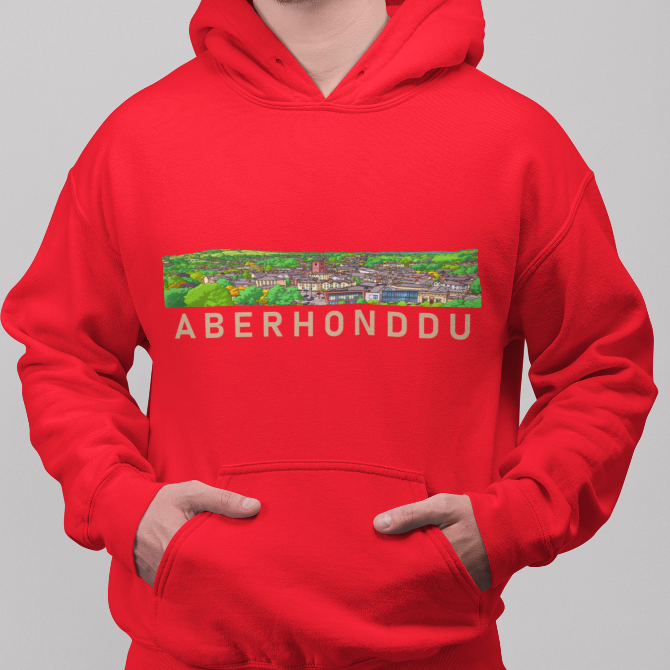 A man wearing a bright red pullover hoodie with a colorful landscape graphic and the text 'ABERHONDDU' across the chest, paired with blue jeans against a solid gray background.