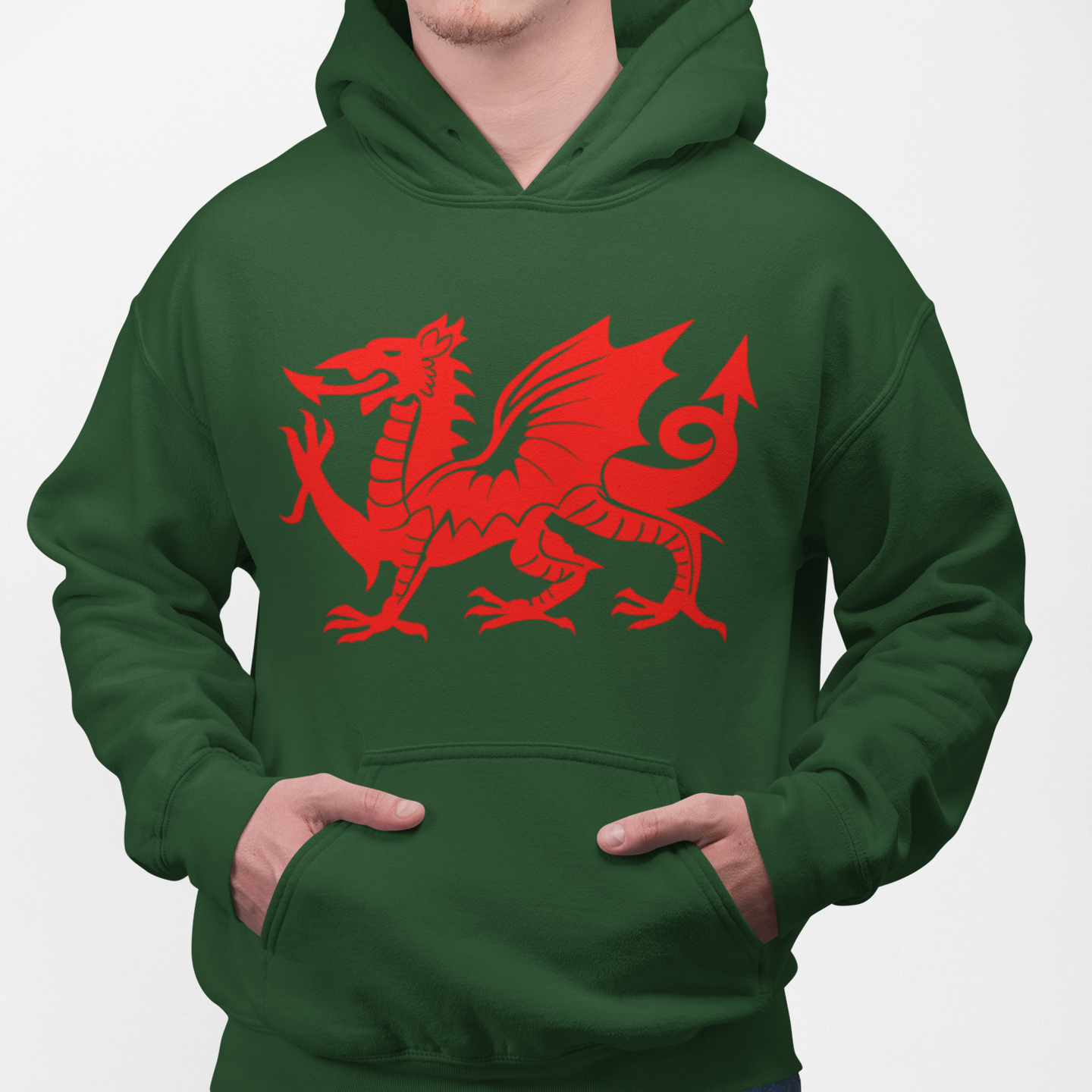 A man wearing a dark green pullover hoodie with a large red Welsh dragon graphic on the chest, paired with blue jeans, against a plain light gray background.