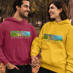 A man and a woman standing in an autumn park, both wearing matching Aberystwyth hoodies. The man's hoodie is magenta, and the woman's is yellow, both featuring a landscape graphic and the text 'ABERYSTWYTH' on the chest.