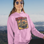 A woman wearing a pink hoodie with a 'Cawl' graphic stands on a mountain peak with a golden retriever dog in the foreground, with a scenic mountain landscape and clouds in the background.