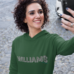 A woman taking a selfie outdoors wearing a dark green hoodie with 'WILLIAMS' printed across the chest in a metallic silver-gray font.