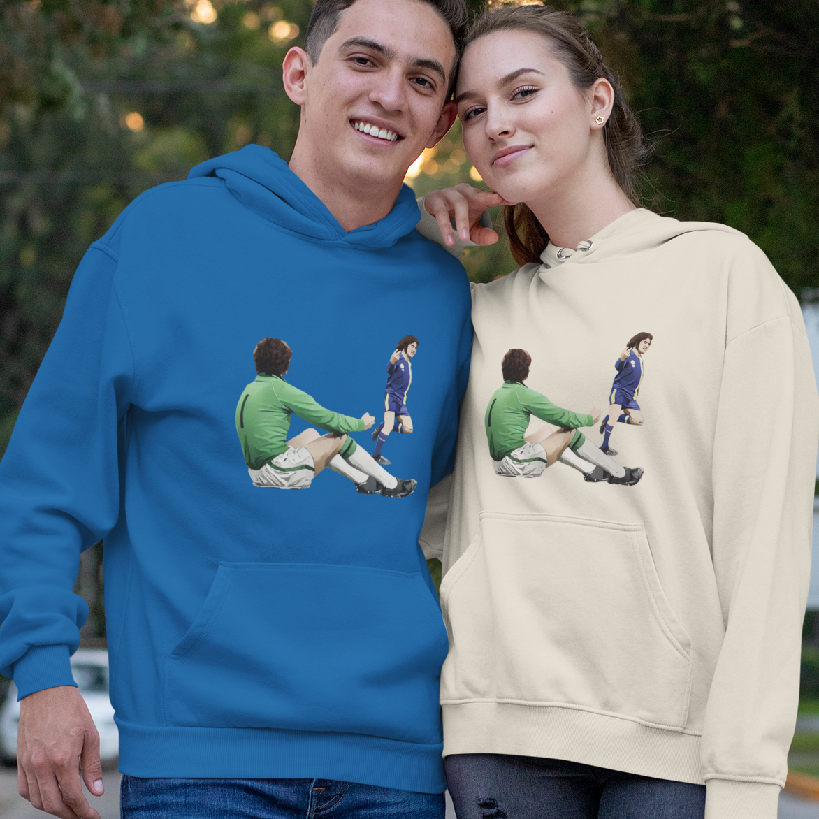 Two people wearing blue and beige hoodies with graphic designs outdoors.