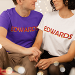 Two people sitting together wearing 'EDWARDS' t-shirts with a festive background.