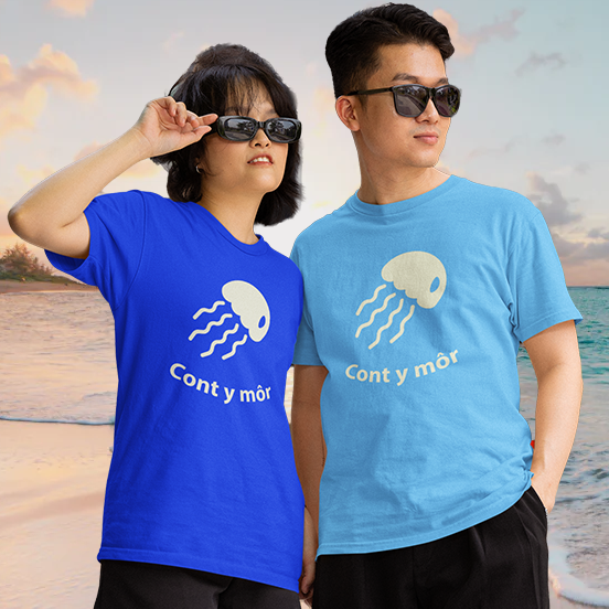 Two people wearing blue t-shirts with a jellyfish design and text on a beach.