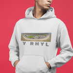 A person wearing a white pullover hoodie with a rectangular scenic graphic on the chest and the text 'Y RHYL' printed below it, posed against a solid red background.