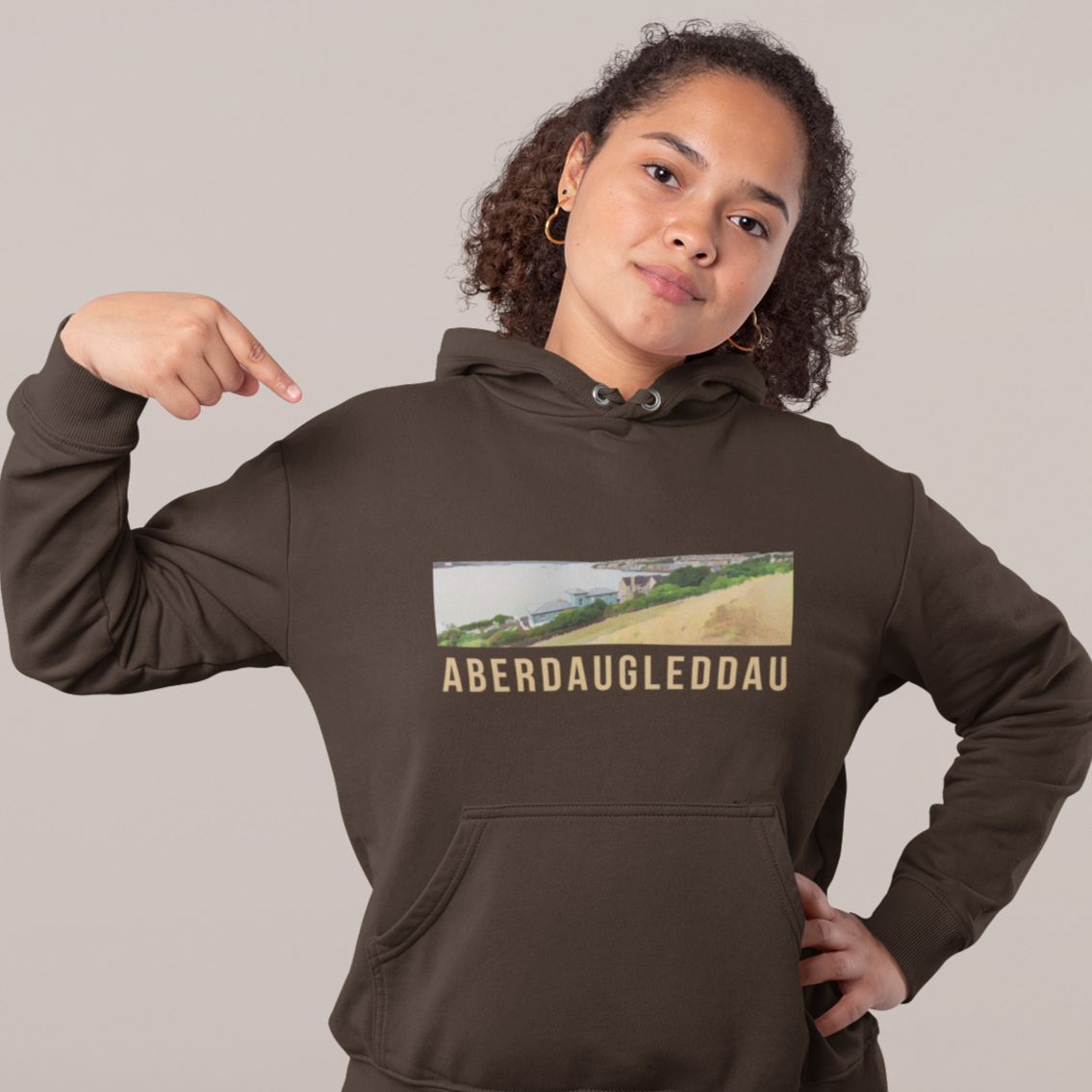 Person wearing a brown hoodie with a graphic and text, pointing at the design.