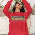 Person wearing a red sweatshirt with 'Aberffraw' text and graphic, sitting on a couch with a decorative plant in the background.