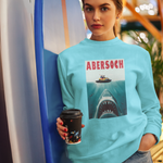 Person wearing a blue sweatshirt with a shark graphic and 'Abersoch' text, holding a coffee cup.
