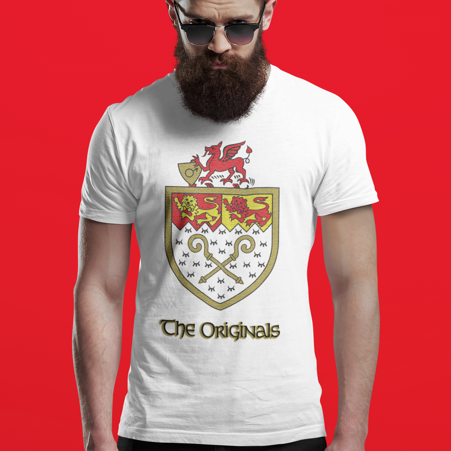 A man with a full beard and sunglasses wearing a white graphic t-shirt with a Welsh coat of arms and the text 'The Originals' against a solid red background.