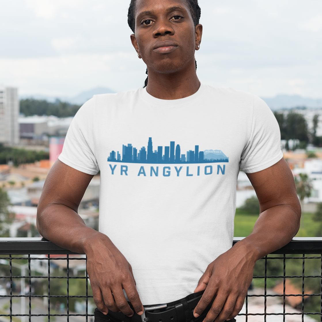 A man wearing a white t-shirt with a blue 'YR ANGYLION' skyline graphic, standing on a balcony with a cityscape background.