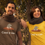 Two smiling people standing outdoors in front of trees, each wearing a matching graphic T-shirt. The shirt design shows a small gray animal sitting in orange mud with the white text 'Cont y cae' below.