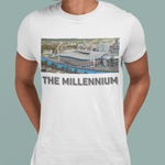 A man wearing a white crewneck t-shirt with a graphic print of a stadium and the text 'THE MILLENNIUM' underneath, paired with dark blue jeans against a solid light green background.
