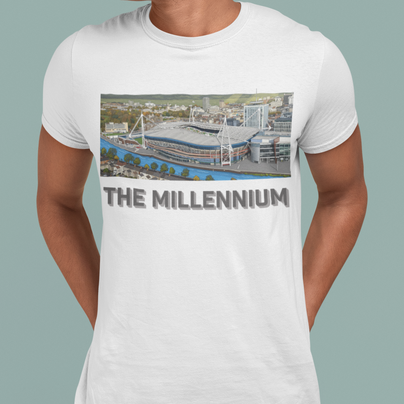 A man wearing a white crewneck t-shirt with a graphic print of a stadium and the text 'THE MILLENNIUM' underneath, paired with dark blue jeans against a solid light green background.