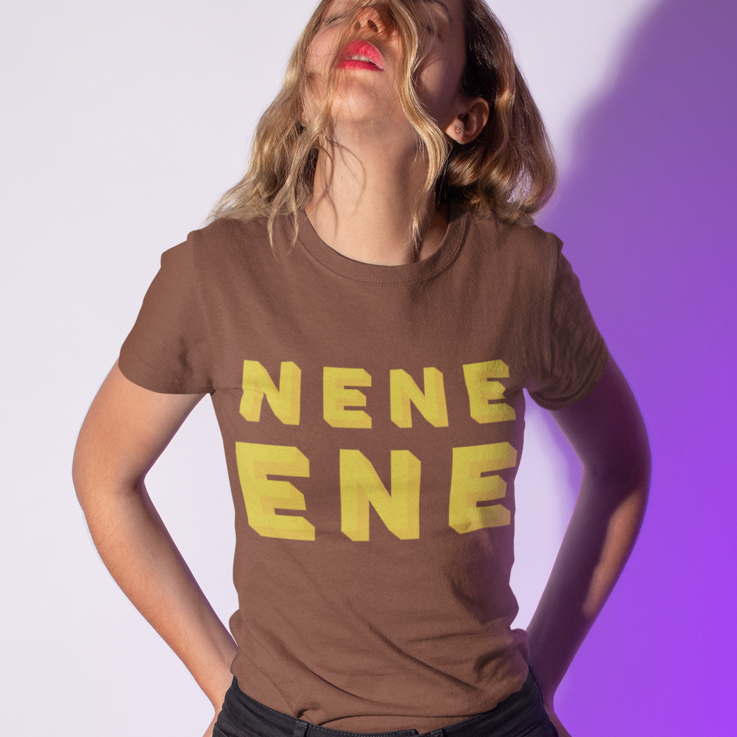 A woman wearing a brown t-shirt with yellow text that reads 'NENE ENE' and black jeans, posing against a white wall with a purple shadow cast on the right.