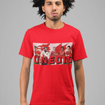 A man with dark curly hair wearing a bright red graphic t-shirt and dark blue jeans, standing against a solid gray studio background. The t-shirt features a rectangular collage graphic of football players with the word 'UNEDIG' printed in bold red letters.