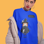 A woman modeling a bright blue oversized graphic T-shirt with a witch character print, styled with a light beige puffer jacket and dark pants against a solid yellow background.