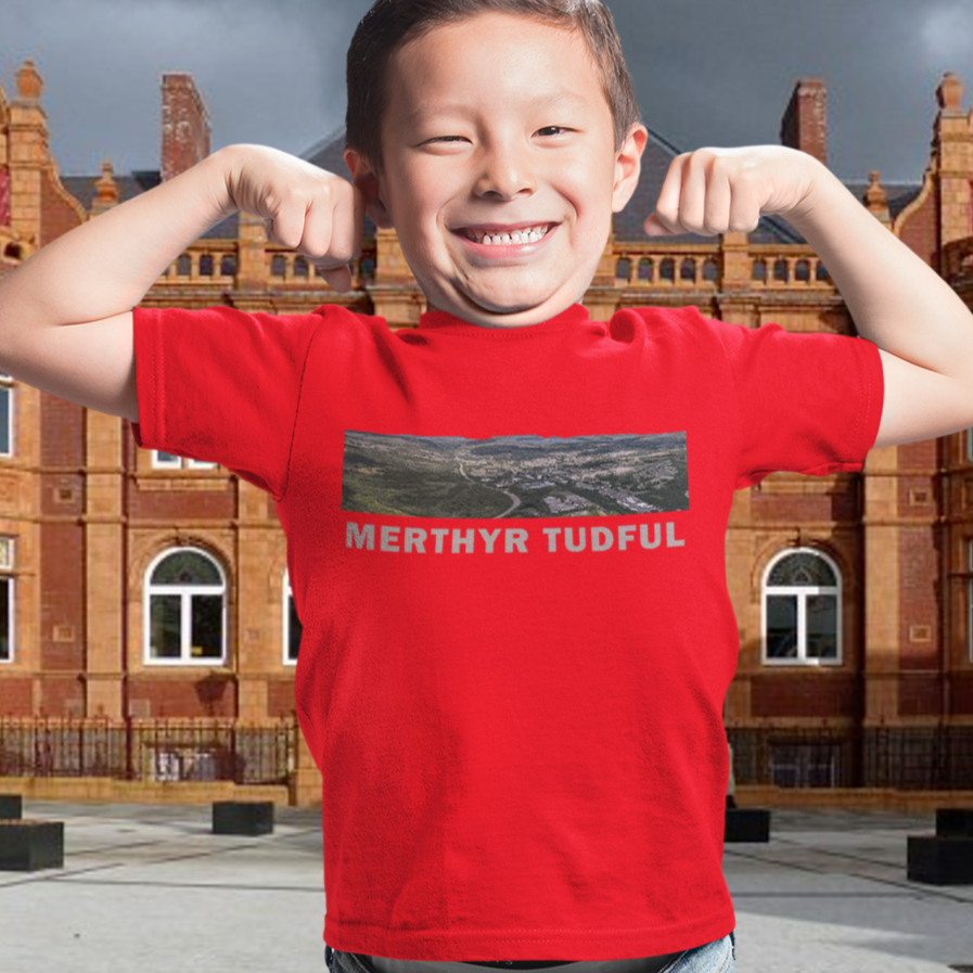 Child wearing a red t-shirt with text in front of a large building