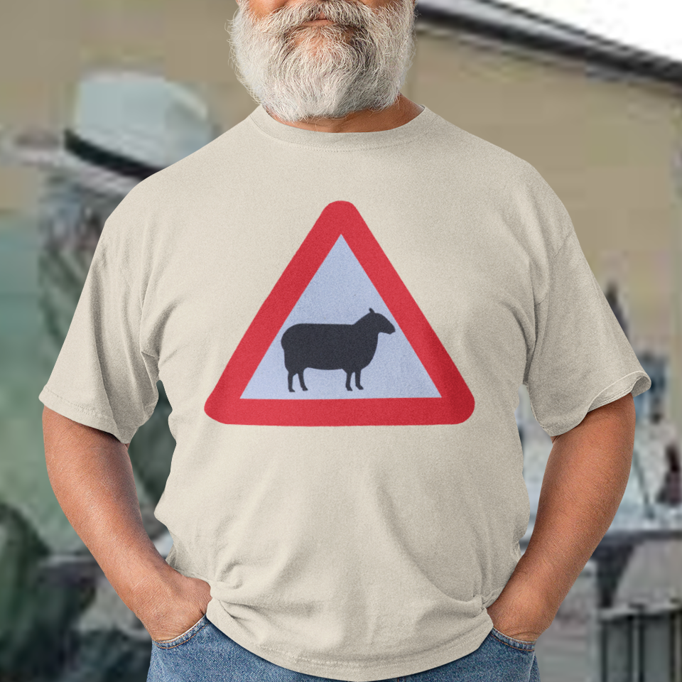 Man wearing a t-shirt with a red and white traffic sign featuring a sheep, standing in front of a building with murals.